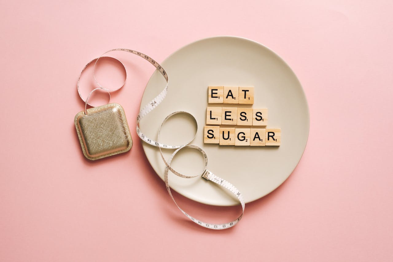 Flat lay of Scrabble tiles saying 'Eat Less Sugar' on a plate with a tape measure on a pink background.